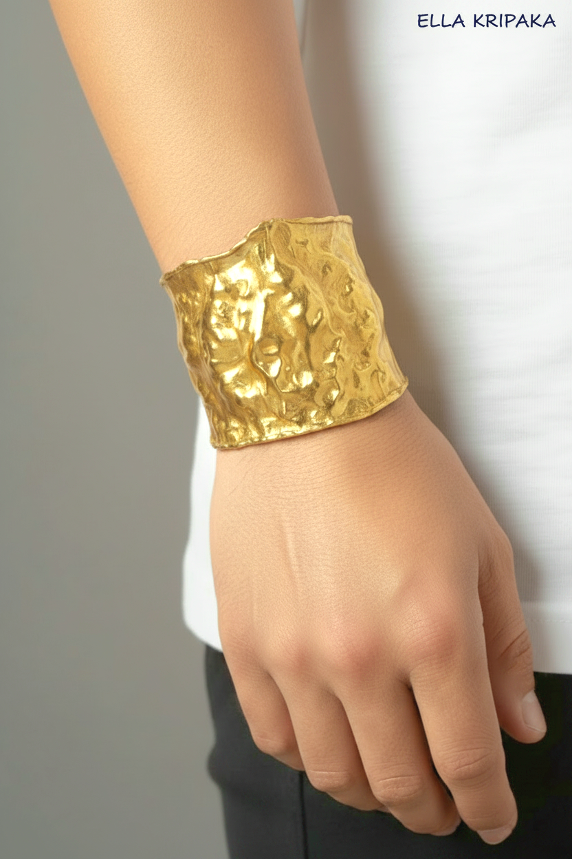 Hammered 24k gold 65mm cuff bracelet with convex uneven textures is worn by a man on wrist and on grey background, and with 'Ella Kripaka' branding