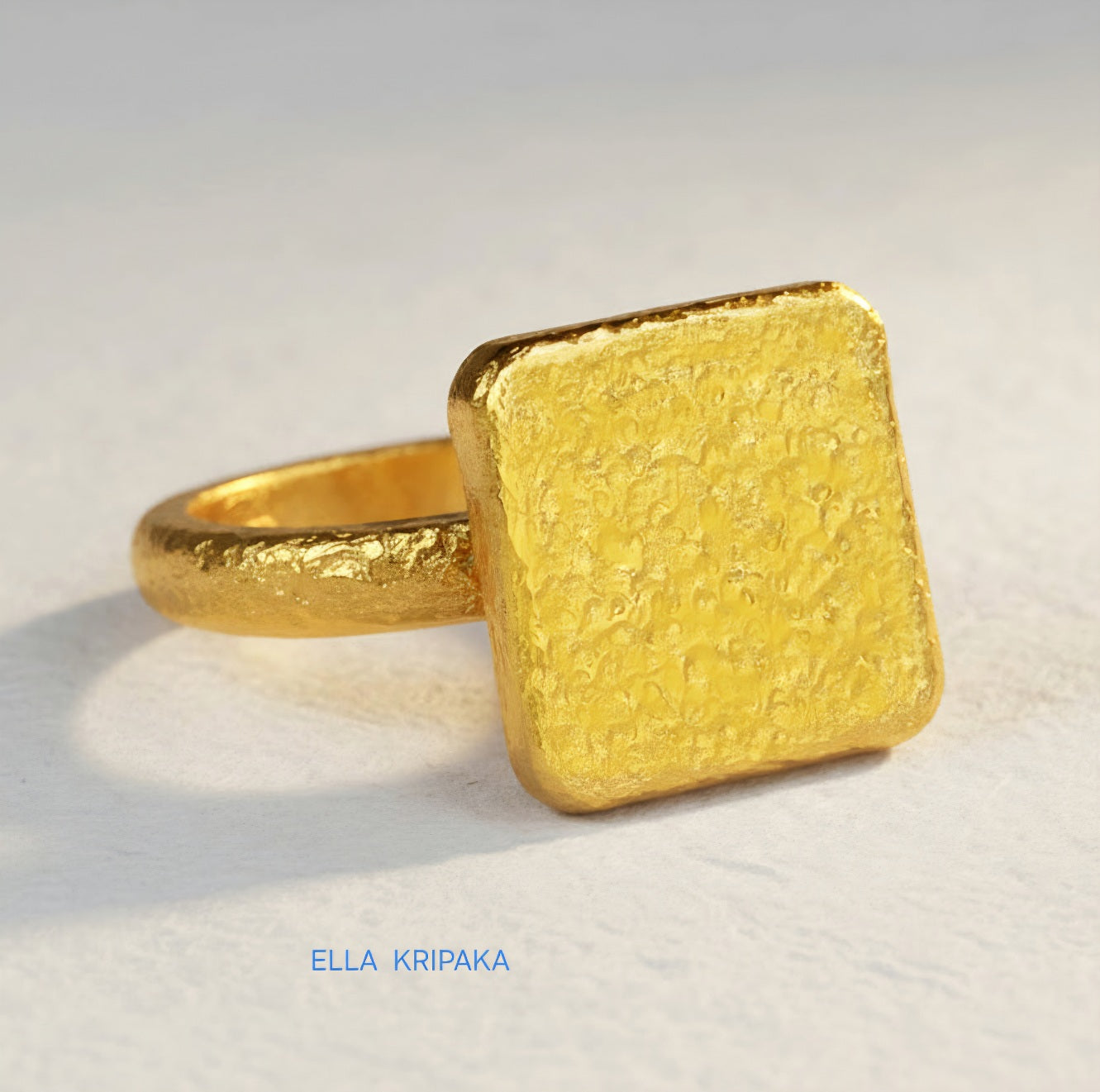 Hammered 24k 9999 Gold thick ring square signet Ancient Rome style with a textured forged gold surface on a white craft paper background, branded 'Ella Kripaka'