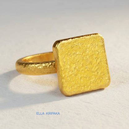 Hammered 24k 9999 Gold thick ring square signet Ancient Rome style with a textured forged gold surface on a white craft paper background, branded 'Ella Kripaka'