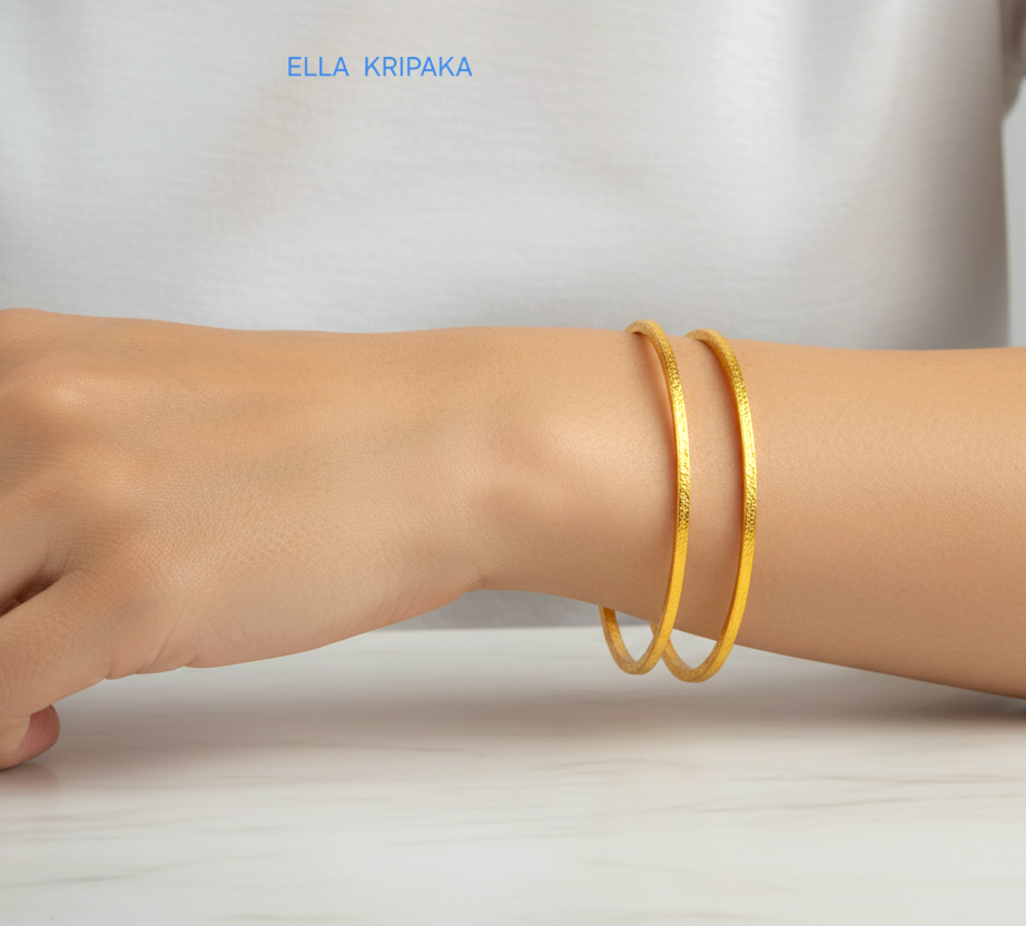 22k gold hammered two thick bangles bracelets Ancient Rome style worn by a woman on wrist and on a white wooden surface, artist-jeweler 'Ella Kripaka' branding