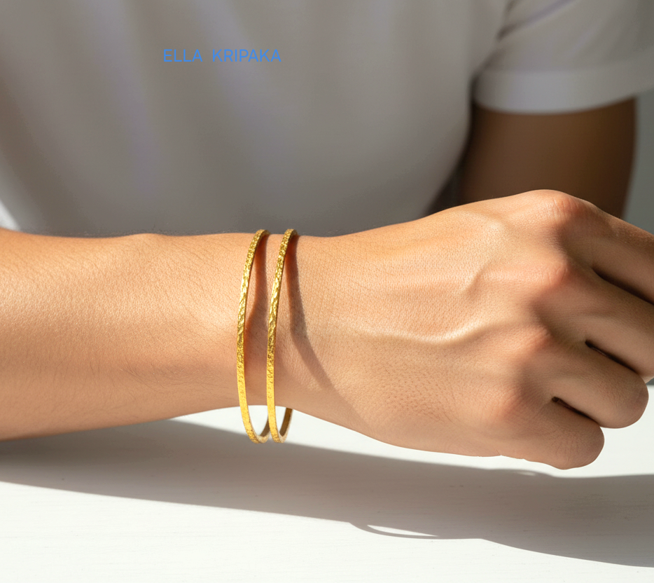 22k gold hammered two thick bangles bracelets Ancient Rome style worn by a man on wrist and on a white wooden surface, artist-jeweler 'Ella Kripaka' branding