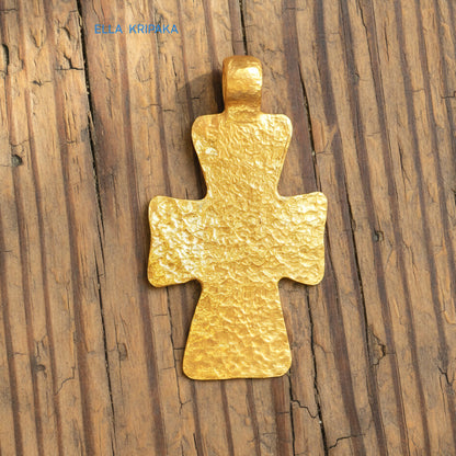 Hammered 24k gold textured cross pendant on rustic old wooden surface, creator artist-jeweler 'Ella Kripaka' branding