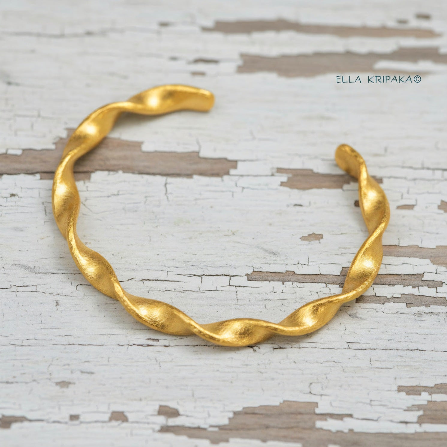 Twisted Viking hammered 24k 9999 gold bracelet cuff on a old white old wooden background, branding artist-jeweler name 'Ella Kripaka'