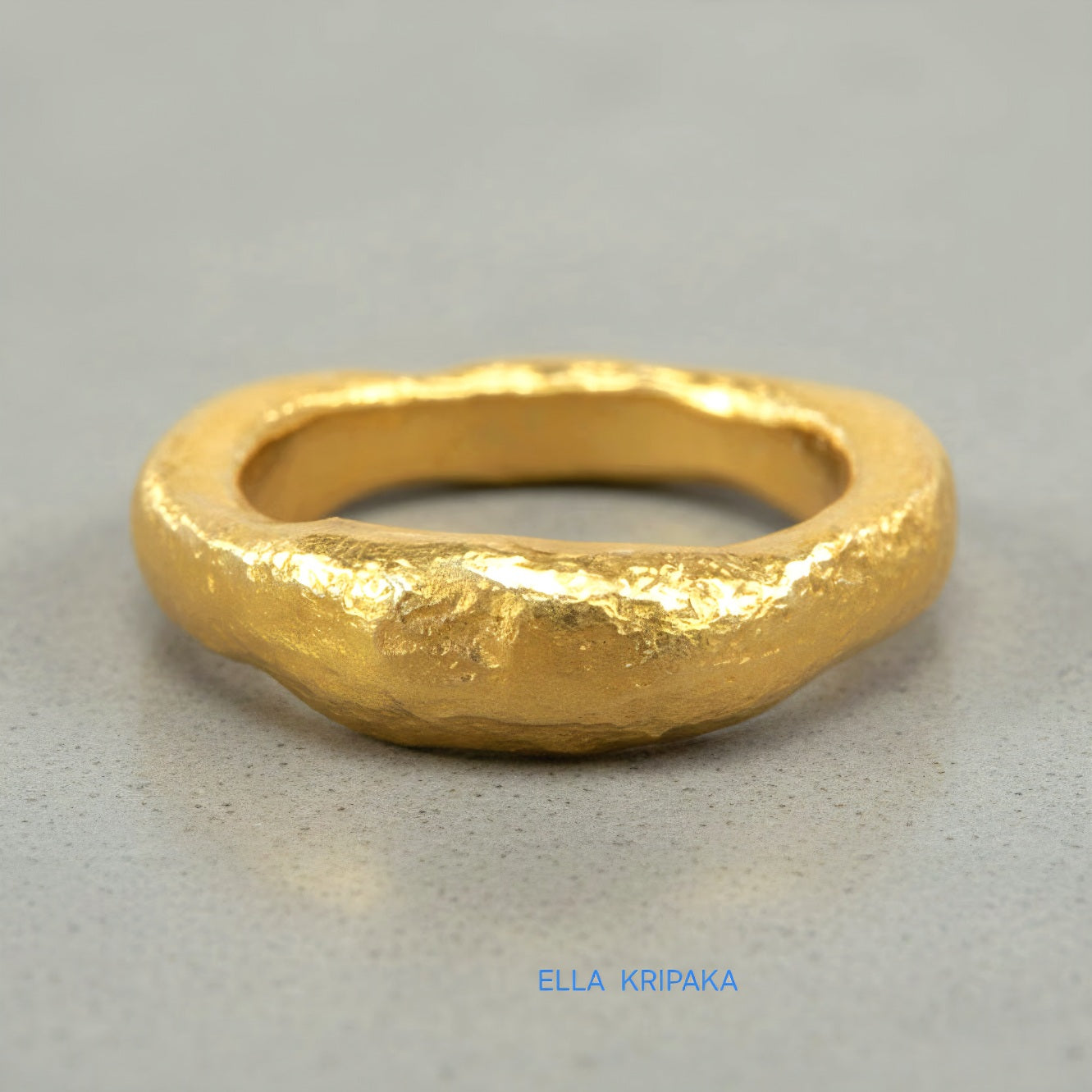 Hammered 24k 9999 Gold thick uneven ring organic signet with a textured gold surface on a grey concrete background, branded 'Ella Kripaka'