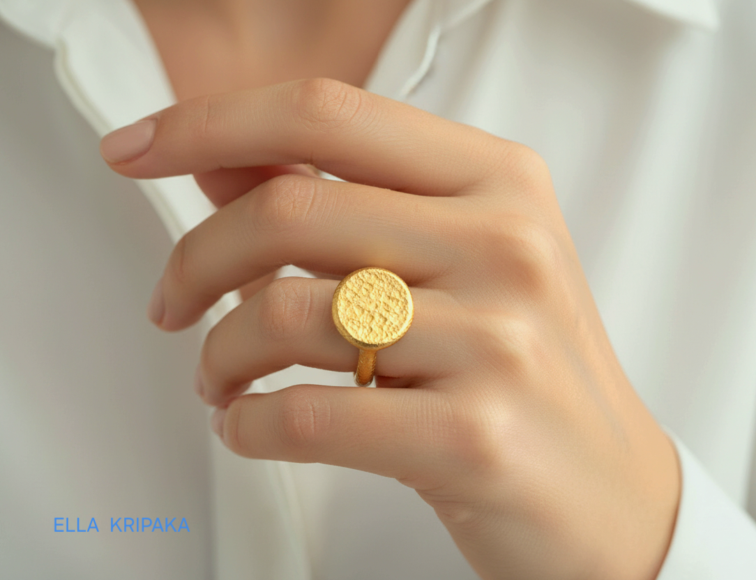 Hammered 24k 9999 Gold thick ring disk signet  Ancient Rome style with a textured forged gold surface worn by a woman on finger and on a white t-shirt background, branded 'Ella Kripaka'