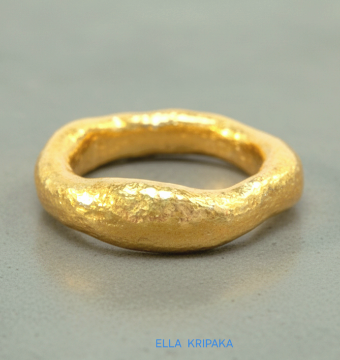 organic hammered 24k Gold thick uneven ring with a textured gold surface on a grey concrete background, branded 'Ella Kripaka'