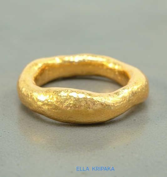 organic hammered 24k Gold thick uneven ring with a textured gold surface on a grey concrete background, branded 'Ella Kripaka'