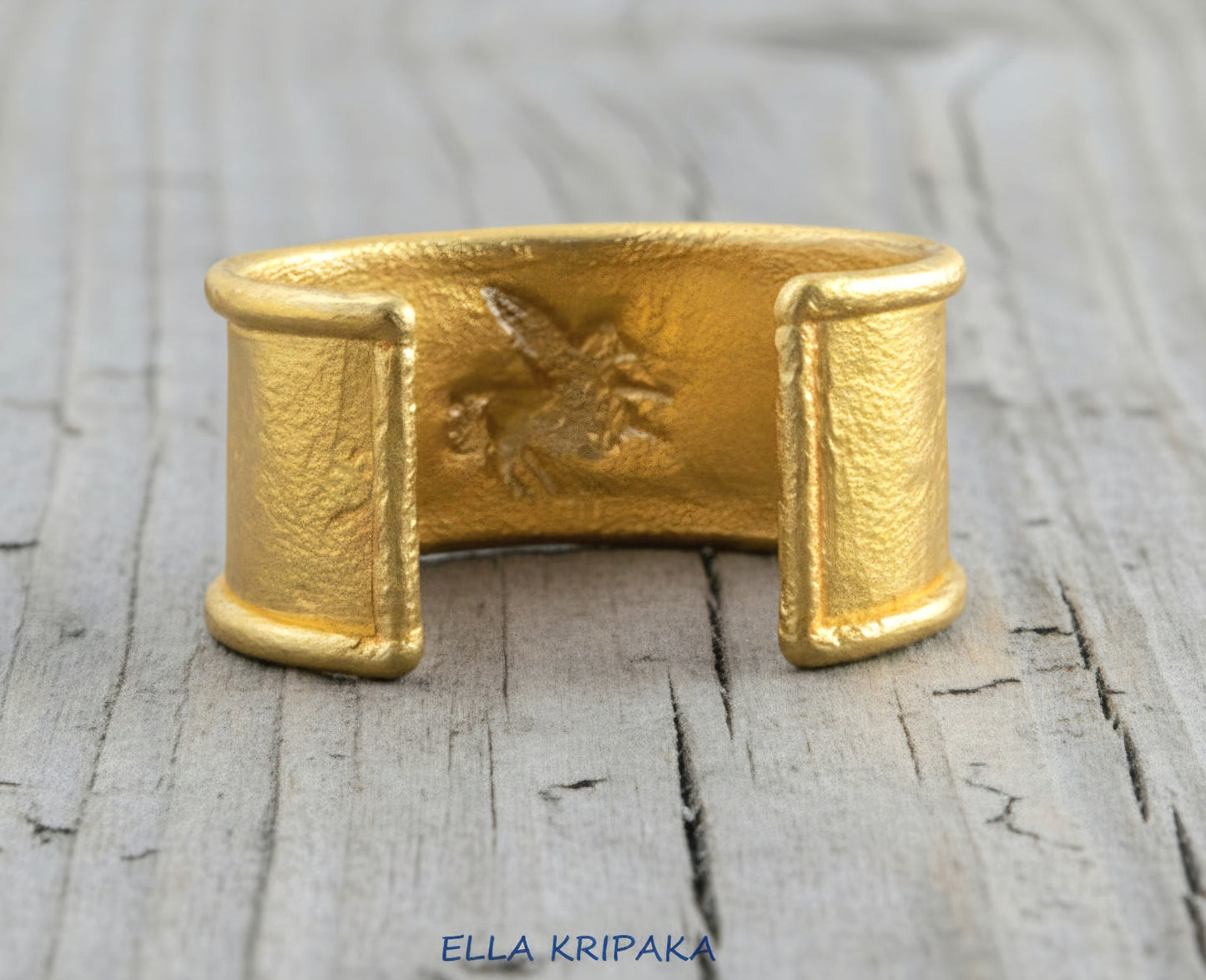 24k 9999 gold hammered Ancient Rome bracelet cuff with convex Pegasus on old wooden background, indicating it is a custom-made jewelry with creator's name 'Ella Kripaka'