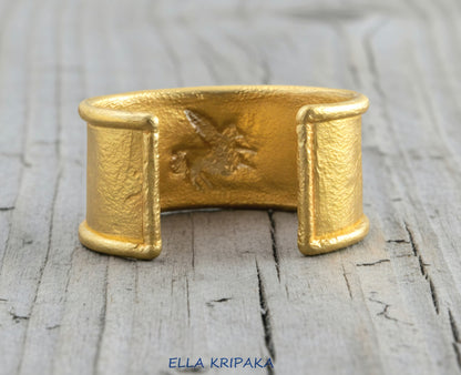 24k 9999 gold hammered Ancient Rome bracelet cuff with convex Pegasus on old wooden background, indicating it is a custom-made jewelry with creator's name 'Ella Kripaka'