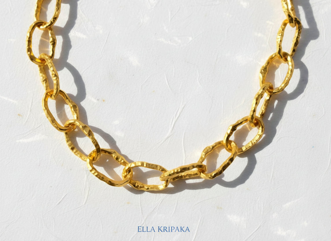 Organic 24k Gold hammered uneven textured chain necklace 12mm of wide and on a white craft paper surface, with artist 'Ella Kripaka' branding