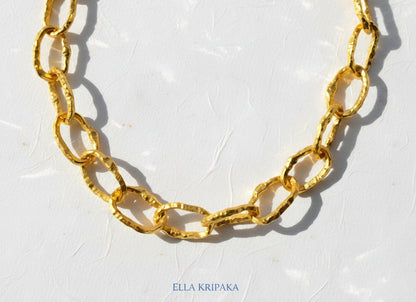 Organic 24k Gold hammered uneven textured chain necklace 12mm of wide and on a white craft paper surface, with artist 'Ella Kripaka' branding
