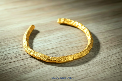 Organic hammered 24k 9999 Gold thick uneven cuff bracelet on a wooden background with 'Ella Kripaka' branding