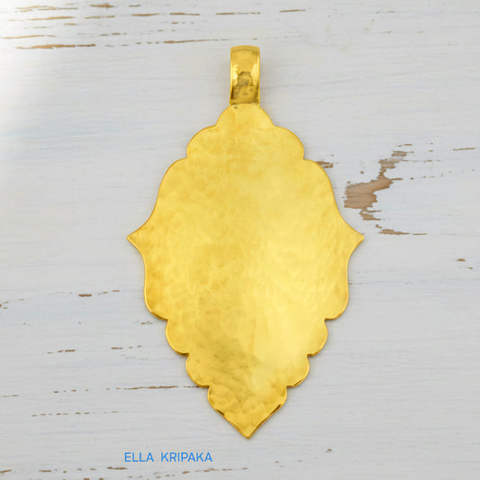 Hammered 24k gold Byzantine ornament pendant on a white rustic wooden surface with 'Ella Kripaka' branding