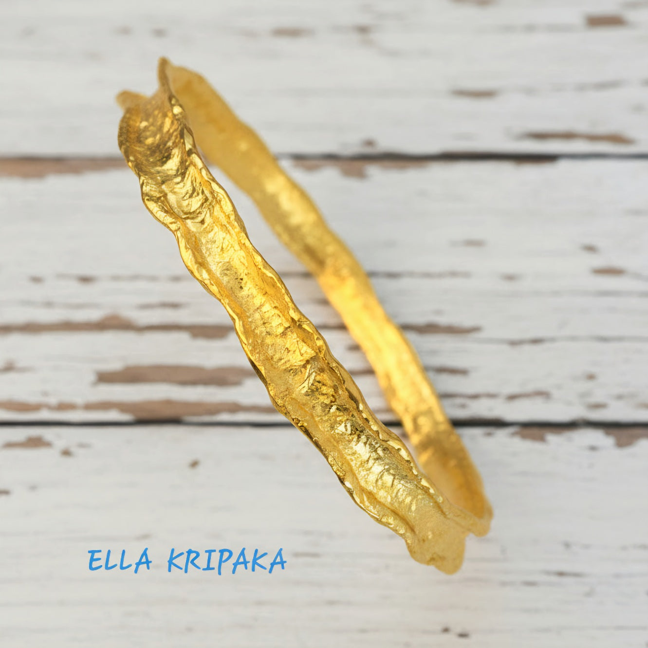 Hammered 22k gold organic textured bangle bracelet with uneven edges on old white wooden surface with 'Ella Kripaka' branding