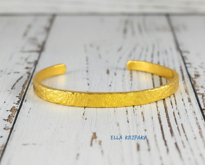 Hammered 24k 9999 gold cuff thick bracelet Ancient Rome style on an old white wooden background, artist-jeweler name 'Ella Kripaka' branding