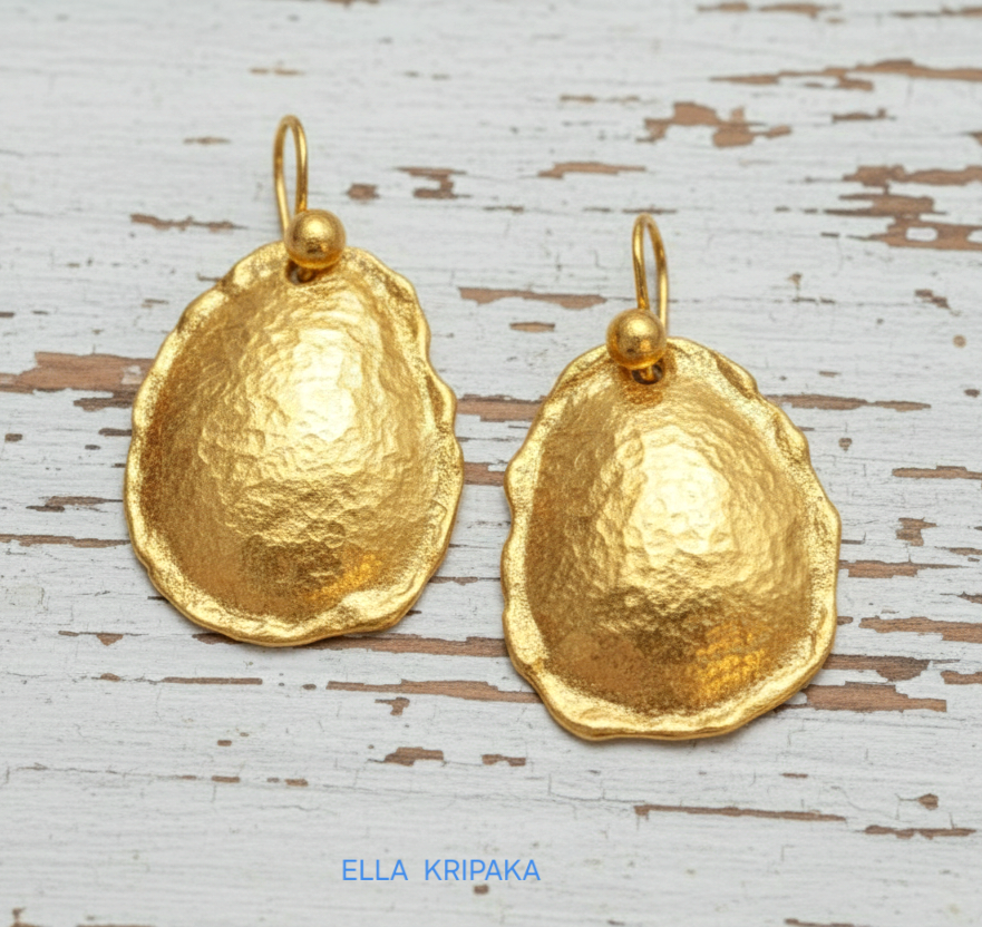 Organic 24k 9999 gold hammered convex oval earrings with thick uneven edges are on old white wooden background, artist-jeweler's name 'Ella Kripaka'