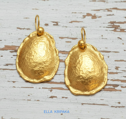 Organic 24k 9999 gold hammered convex oval earrings with thick uneven edges are on old white wooden background, artist-jeweler's name 'Ella Kripaka'