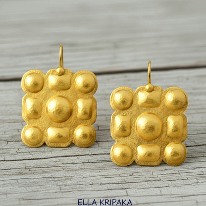 Hammered 24k gold Byzantine square earrings with shiny forged gold textures on old wooden surface, artist-jeweler 'Ella Kripaka' branding