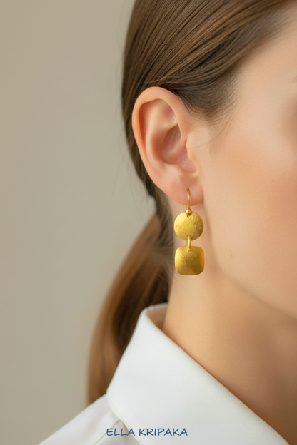 Hammered 24k gold dangling earrings with convex disks and squares are worn by a woman and on light grey background, branding artist-jeweler 'Ella Kripaka'