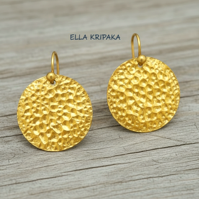 Organic ammered 24k gold, pure 9999 gold disk earrings with shiny forged gold textures on old wooden surface, artist-jeweler 'Ella Kripaka' branding