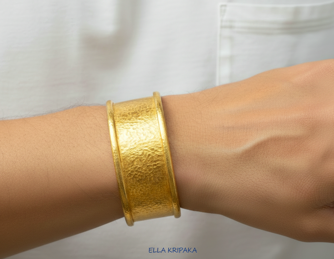 Hammered 24k 9999 gold bracelet cuff Ancient Rome style on person's wrist and with blurred light background with 'Ella Kripaka' branding