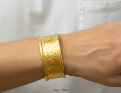Hammered 24k 9999 gold bracelet cuff Ancient Rome style on person's wrist and with blurred light background with 'Ella Kripaka' branding