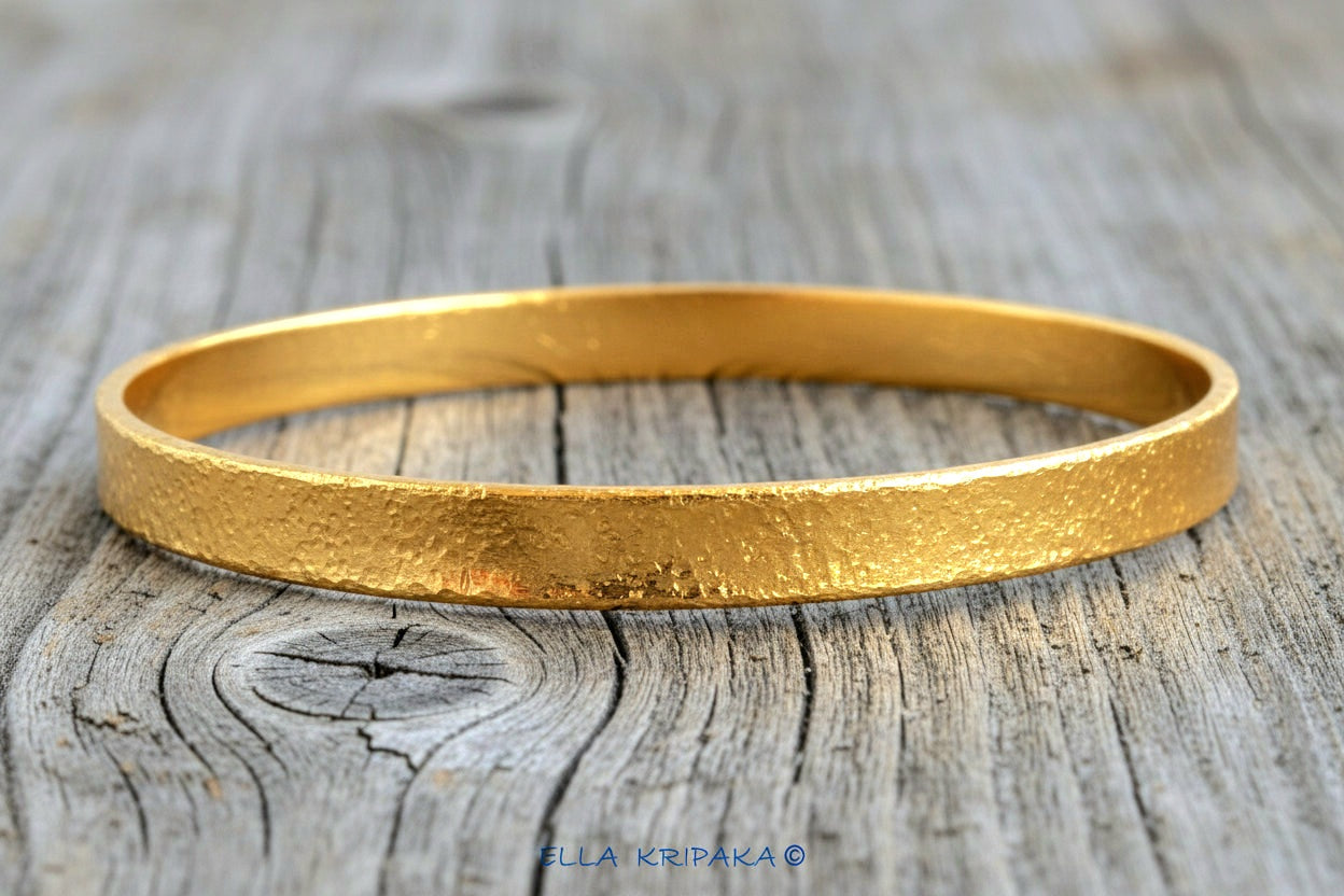 Hammered 24k 9999 gold bangle thick bracelet Ancient Rome style on an old wooden background, artist-jeweler name 'Ella Kripaka' branding