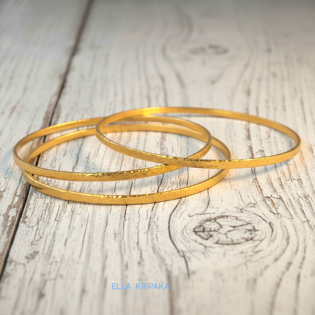 Hammered 22k gold three textured bangles bracelets Ancient Rome style on old white wooden surface with 'Ella Kripaka' branding