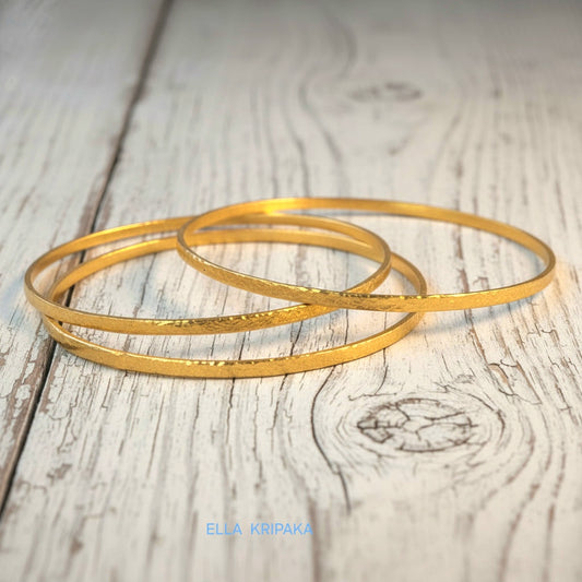 Hammered 22k gold three textured bangles bracelets Ancient Rome style on old white wooden surface with 'Ella Kripaka' branding