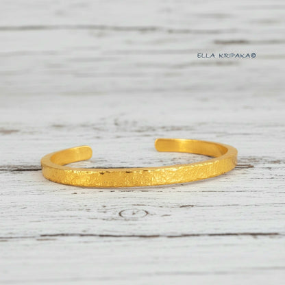 Hammered 24k 9999 gold cuff thick bracelet Ancient Rome style on an old white wooden background, artist-jeweler name 'Ella Kripaka' branding