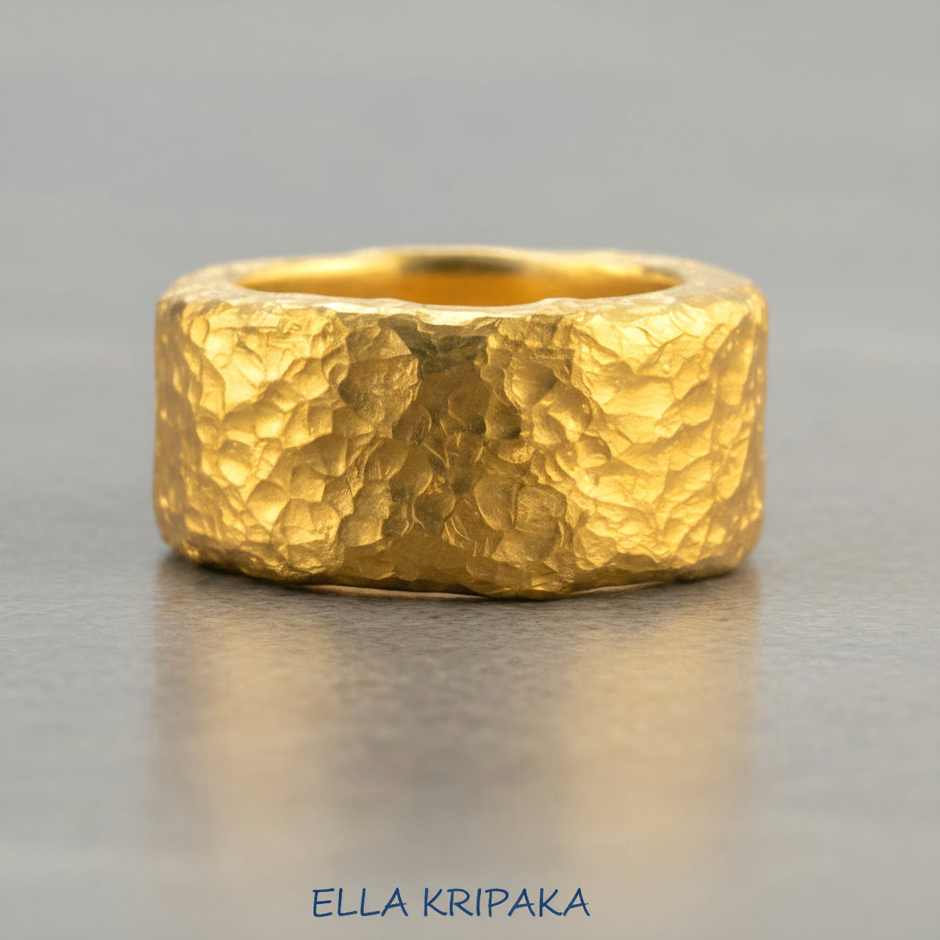 Hammered 24k 9999 Gold thick ring Ancient Rome style with textured gold on a grey concrete background, branded 'Ella Kripaka'