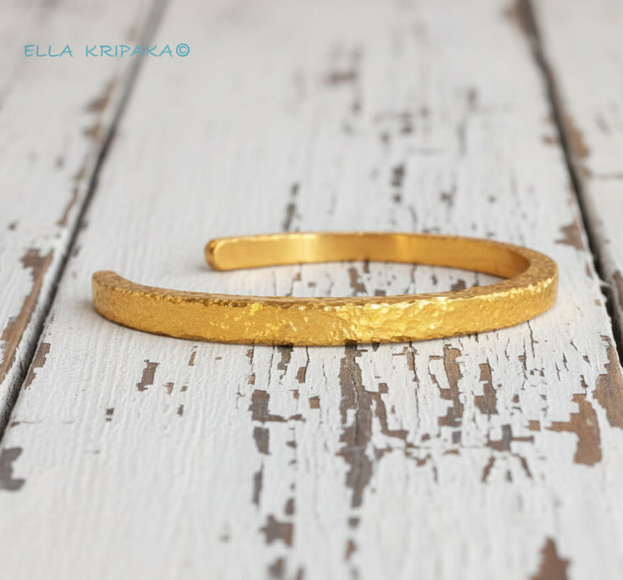 Hammered 24k 9999 gold cuff thick bracelet Ancient Rome style on an old white wooden background, artist-jeweler name 'Ella Kripaka' branding