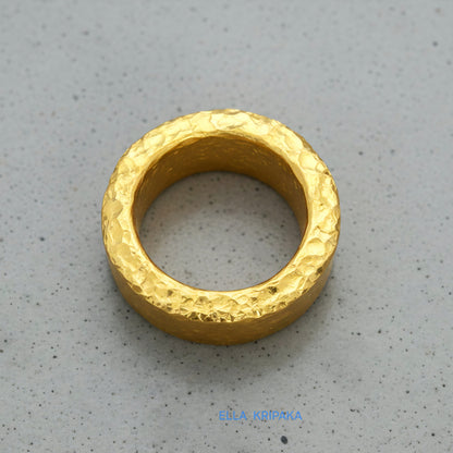 Hammered 24k 9999 Gold thick ring Ancient Rome style with textured gold on a grey concrete background, branded 'Ella Kripaka'