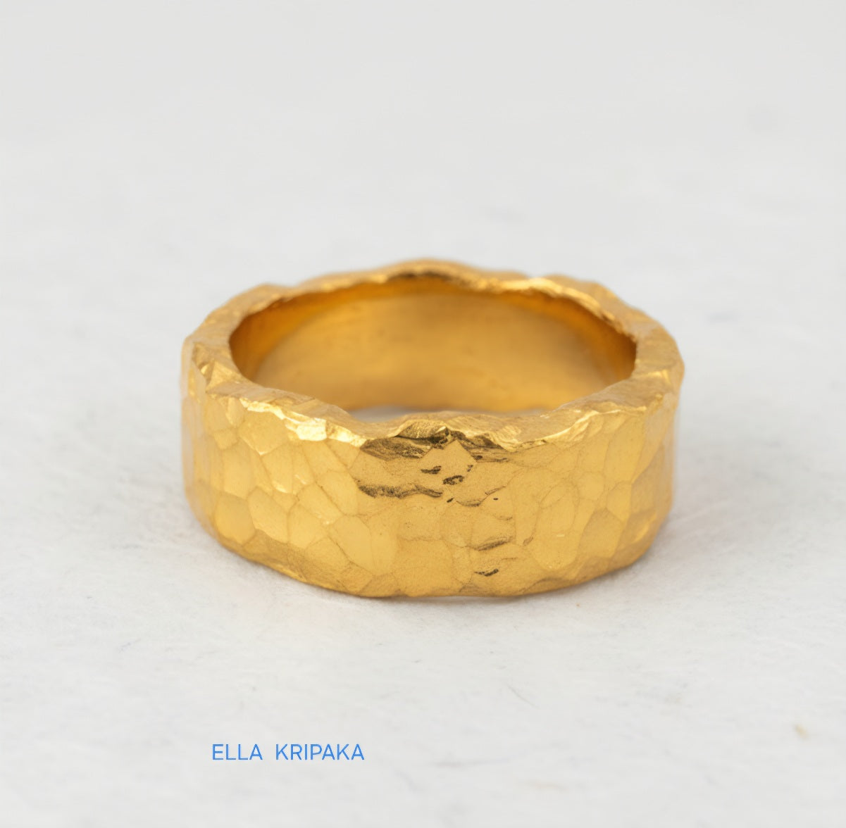Organic hammered 24k 9999 Gold ring with uneven edges on white paper surface, artist-jeweler's name 'Ella Kripaka' is written in picture