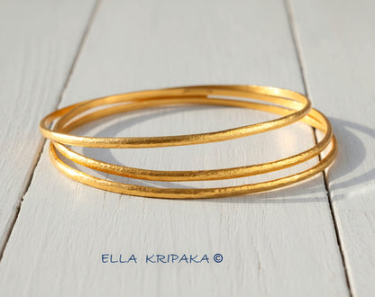 Hammered 22k gold three textured bangles bracelets Ancient Rome style on white wooden surface with 'Ella Kripaka' branding