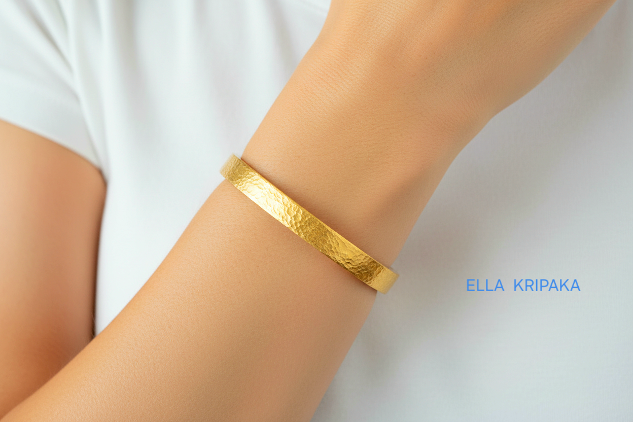 Hammered 24k 9999 gold bangle thick bracelet Ancient Rome style worn by a woman on hand and on a white t-shirt background, artist-jeweler name 'Ella Kripaka' branding