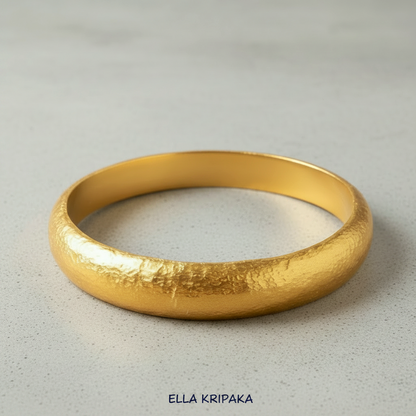Hammered 24k gold bangle thick bracelet with rounded edges on grey concrete background, and artist-jeweler 'Ella Kripaka' branding