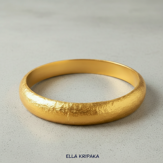 Hammered 24k gold bangle thick bracelet with rounded edges on grey concrete background, and artist-jeweler 'Ella Kripaka' branding