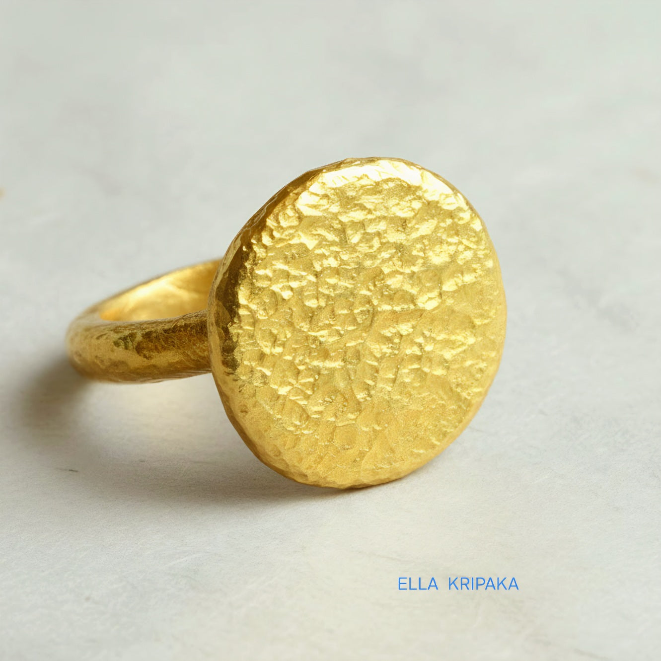 Hammered 24k 9999 Gold thick ring disk signet Ancient Rome style with a textured forged gold surface on a white craft paper background, branded 'Ella Kripaka'