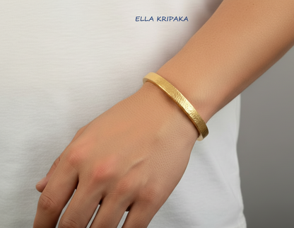 Hammered 24k 9999 gold cuff thick bracelet Ancient Rome style  worn by a man in white t-shirt and on grey background, artist-jeweler name 'Ella Kripaka' branding