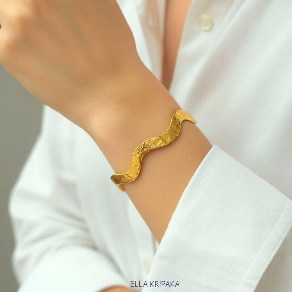 24k gold hammered bracelet textured bangle with wavy design is wearing on woman's hand and on white shirt background, branded 'Ella Kripaka'