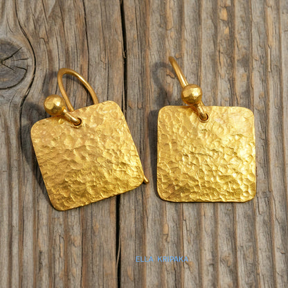 Hammered 24k gold, pure 9999 gold square earrings with shiny forged gold textures on old wooden surface, artist-jeweler 'Ella Kripaka' branding