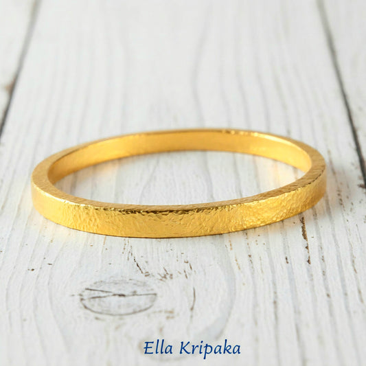 Hammered 24k 9999 gold bangle thick bracelet Ancient Rome style on a white old wooden background, artist-jeweler name 'Ella Kripaka' branding