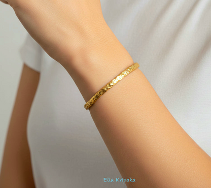 Organic 24k gold textured bangle thick bracelet with uneven edges worn by a woman on hand and on a white background, artist-jeweler name 'Ella Kripaka'