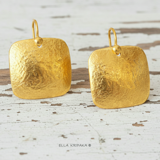 Solid 24k 9999 gold hammered Byzantine convex square earrings with hook clasps and shiny forged gold textures on white old wooden background , artist's name 'ELLA KRIPAKA'