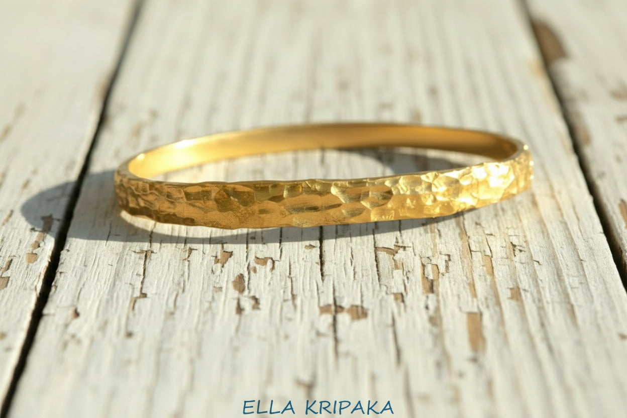 Organic hammered 24k 9999 Gold thick bangle uneven bracelet on a wooden background, artist's name 'Ella Kripaka' branding