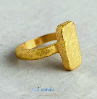 Hammered 24k 9999 Gold thick ring square signet Ancient Rome style with a textured forged gold surface on a white craft paper background, branded 'Ella Kripaka'