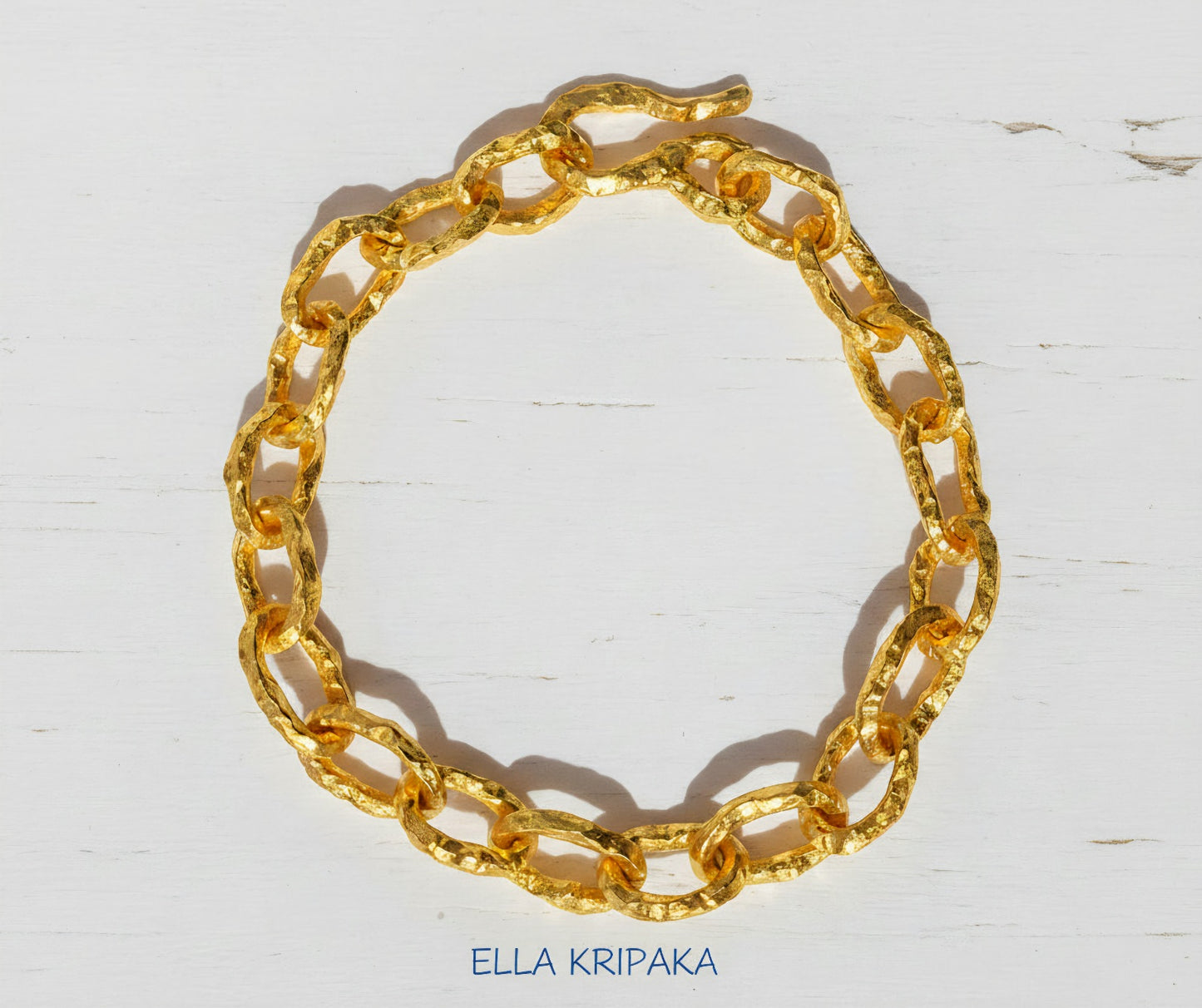 Hammered 24k 9999 gold organic bracelet chain with hammered uneven textures and a thick hook clasp on white wooden surface, artist name 'Ella Kripaka'