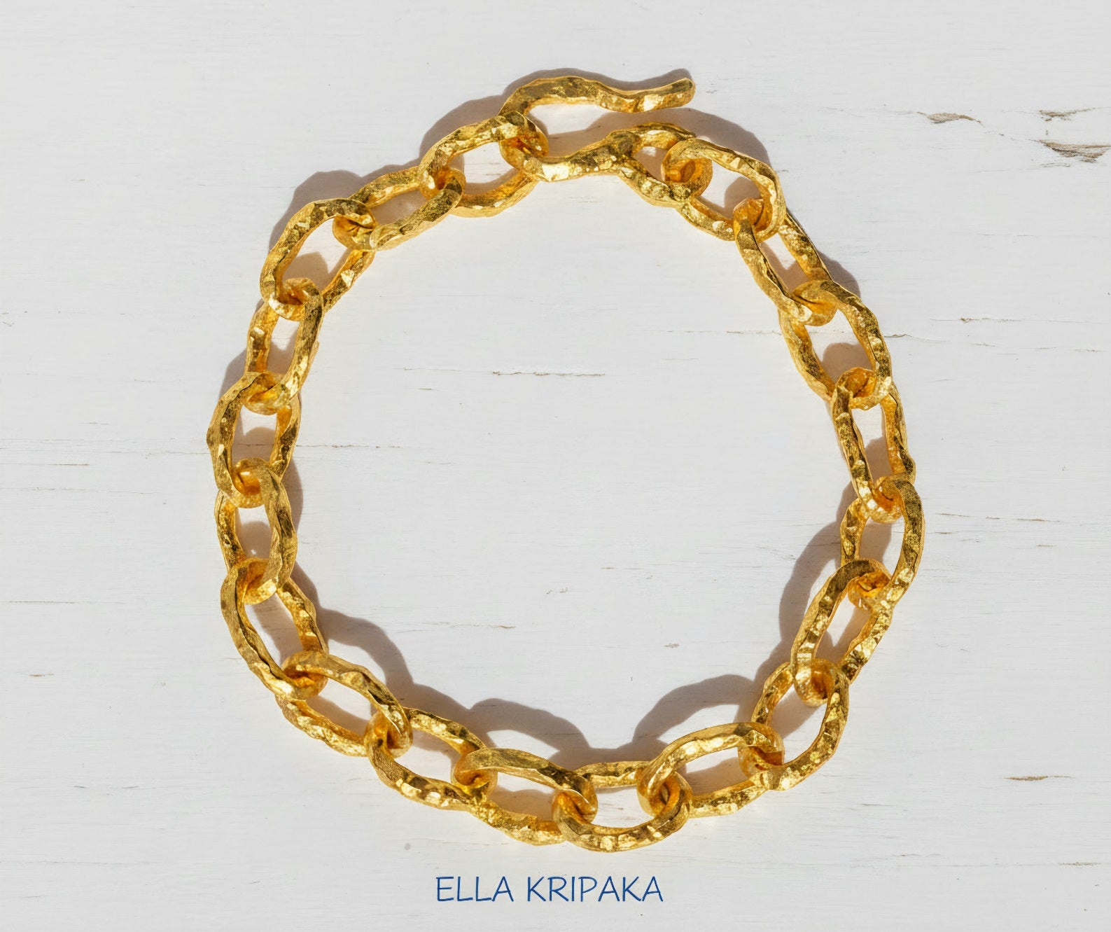 Hammered 24k 9999 gold organic bracelet chain with hammered uneven textures and a thick hook clasp on white wooden surface, artist name 'Ella Kripaka'