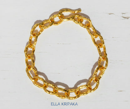 Hammered 24k 9999 gold organic bracelet chain with hammered uneven textures and a thick hook clasp on white wooden surface, artist name 'Ella Kripaka'